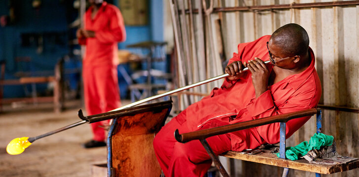 Glassblowing, heat and shape with black man artisan in forge or foundry for industrial production. Artistic, creative and design with professional glassblower in plant or workshop for manufacturing