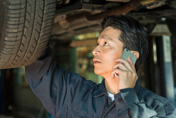 自動車点検をしながら電話で話す40代男性整備士