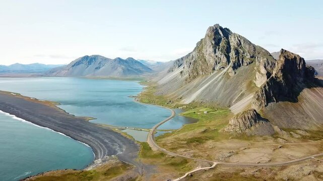 A stunning view of the rugged mountain and serene coastline of Hvalnes, Iceland. The landscape features dramatic cliffs, calm blue waters, and a winding road that blends into the natural beauty