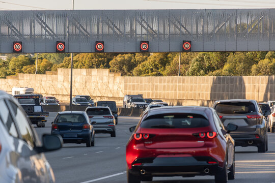 Highway traffic with multiple red 80km/h speed limit signs mounted on an overhead gantry, with various cars driving on the multi-lane motorway.Melbourne Australia.