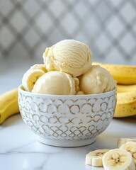 Creamy banana ice cream scoops in decorative bowl with fresh bananas on marble surface