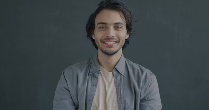 Slow motion portrait of joyful Middle Eastern man waving hand smiling on black background. Nonverbal communication and hello gesture concept.
