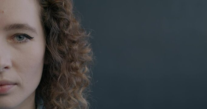Close-up portrait of insecure and confused young woman half face looking at camera on black color background. People and emotion concept.