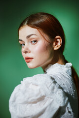 A young woman with shoulder length brown hair in a vintage white blouse poses against a soft green...