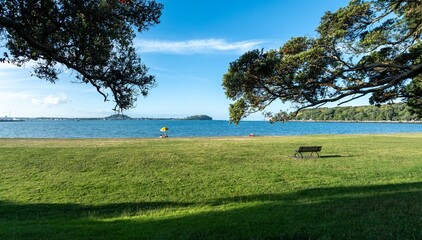 Relaxing by the water. People sunbathe under a yellow umbrella on a grassy waterfront. Tranquil...