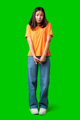 Young woman in orange shirt stands awkwardly against green backdrop in indoor studio