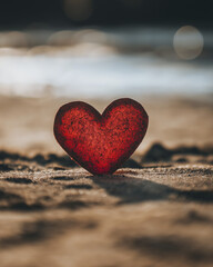 Fototapeta premium red heart shaped paper cut out on beach, symbolizing love and connection. soft sand and gentle light create serene atmosphere