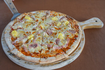 Homemade pizza with tomatoes, mozzarella and ham. Homemade Pizza on a rustic wooden table. Hot pizza slice with melting cheese on a rustic wooden plate.