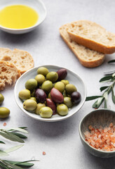 Green and black olives with olive oil, bread and himalayan pink salt on grey table