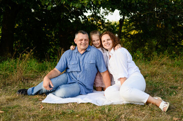 Portrait of happy family in park. Mom and dad with baby girl sitting on grass during picnic...