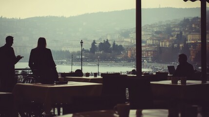 Silhouetted figures are seated at an outdoor cafe overlooking a hazy coastal city. The background shows a blurred cityscape and calm water, bathed in