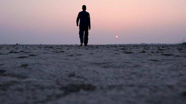 man walking at dry cracked farm fields with sunrise orange sky at dawn close up view from low angle