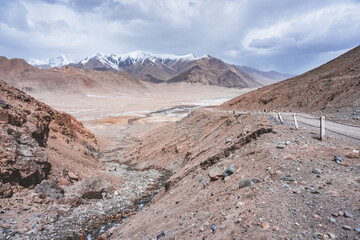 Dusty high-mountain road of Pamir Highway and Ak-Baital Pass, panoramic landscape in rocky mountains with snow in Tien Shan Mountains in Tajikistan