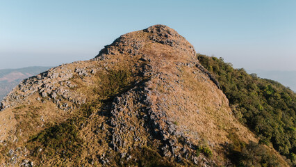 A rocky hilltop with sparse vegetation, showcasing a clear sky and a distant landscape, ideal for outdoor activities or photography.