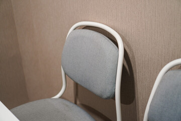 Two grey fabric chairs with white metal frames rest against a neutral wall. A simple, minimalist...