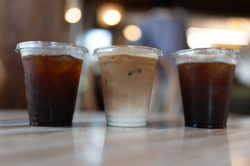 A row of three plastic take away cup of iced black coffee americano and iced coffee latte on table in coffee shop