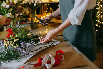 A florist works on preparing beautiful floral arrangement. Various flowers and materials lie on table, emphasizing the artistic and inspiring atmosphere associated with floral design and presentation.