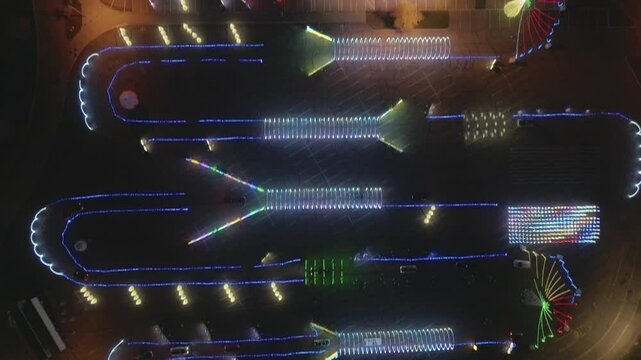 A drone flies overhead, providing a bird's-eye view of a vibrant drive-through Christmas lights display, featuring twinkling decorations and a festive atmosphere.