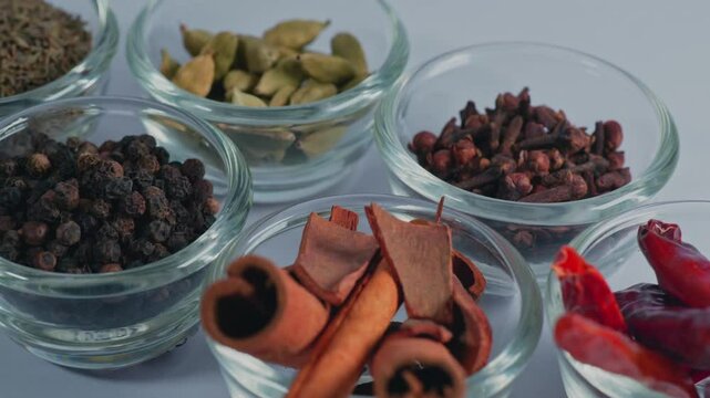 different types of whole spices Erra Mirapakayalu, Dalchina Chekka, Lavangalu, Miriyalu, Yalakulu and Seema Sopyginjale in small glass bowl, 4k, semi circle shot