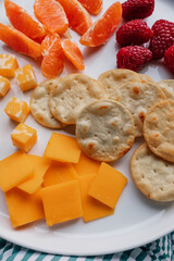 cheddar, colby jack, crackers, raspberries, orange segments on white plate