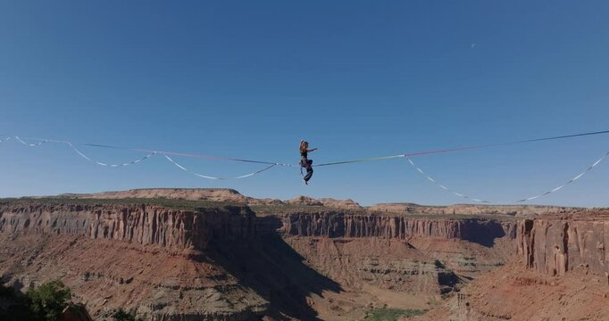 Aerial view of woman standing up on highline slackline over desert canyon