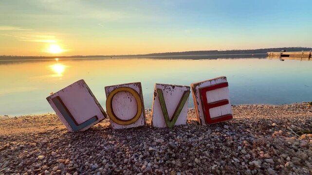 colorful wooden love word in the sand on the beach in romantic sunset light
