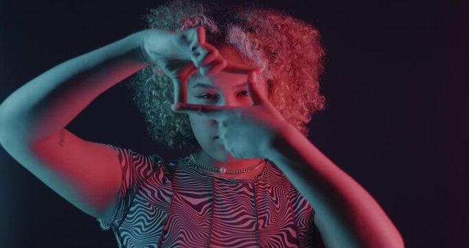 Creative African American woman making view finder hand gesture in neon light on dark background. People and signs concept.