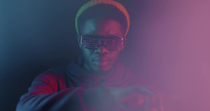 Stylish African American man dancing gesturing looking at camera in neon light on dark background. Entertainment and nightlife concept.
