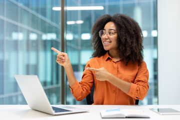 Businesswoman at workplace inside office, pointing with hands and fingers to the side, joyful...