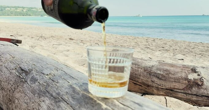 Whiskey is poured into a glass. Whiskey is poured into a glass against the background of the beach. Alcohol is poured into a glass on the beach.