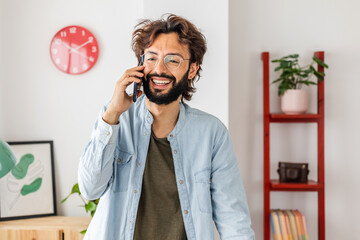 Young happy creative man talking on phone in the office. Freelance business male having conversation on cell phone.