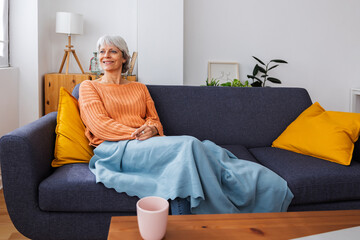 Obraz premium Happy senior adult woman covered with a blanket enjoying being at home on a cold winter day while looking out at the street
