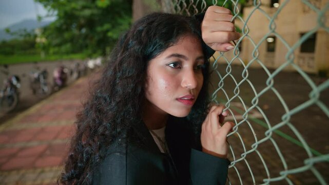 Girl lean against a chain link lost in deep thought