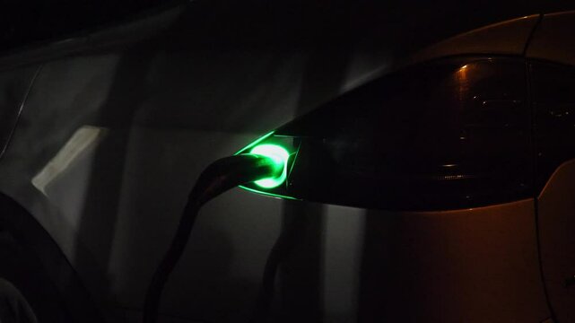 Electric car charging at evening. Power connector inserted into EV automobile. Process of recharging of e-vehicle battery. Environmentally friendly zero emission auto. Clean energy filling technology
