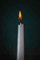 A burning white candle. The flame glows brightly and vibrantly. The background is dark, enhancing the contrast between the light of the flame and the surrounding darkness.