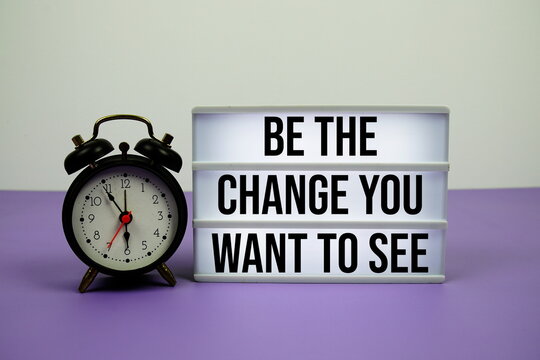 Be the change you want to see text on LED lightbox with alarm clock on purple background