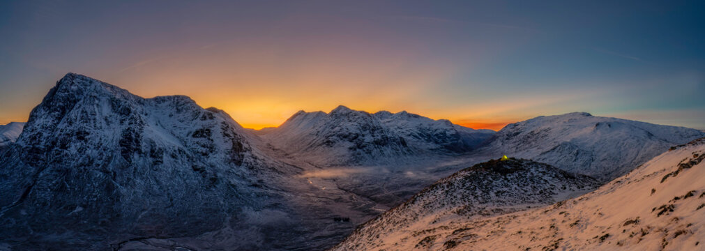 View into Glencoe, Highlands, Scotland. A lone tent wild camping on the peak over looking Glencoe at sunset.