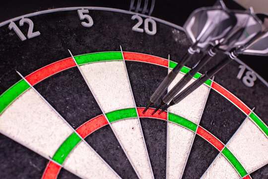 Official dartboard with closeup view of three darts sticking in the Triple Twenty