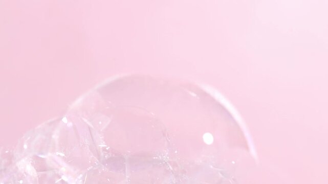 Soap bubbles burst, bath foam close-up on pink background.