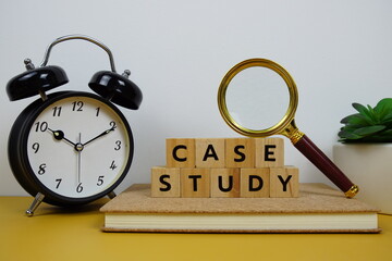 Magnifying glass and alarm clock with wooden blocks alphabet letters CASE STUDY text message on yellow background