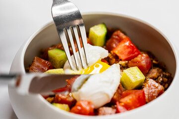 A delicious close-up of a gourmet dish featuring a poached egg on a bed of diced tomatoes, avocado, and crispy bacon, garnished with fresh herbs. Perfect for food lovers and culinary visuals.