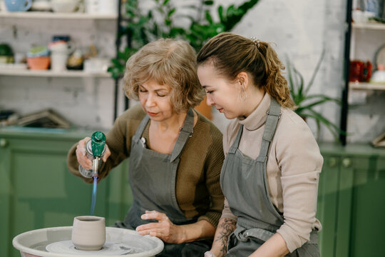 Hands-on learning, senior woman mastering pottery techniques using rotating wheel Mentor teaches pottery fundamentals, demonstrating sculpting skills on an electric wheel