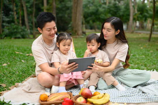 Warm and loving family spending time together at a park picnic and using digital tablet for entertainment or learning