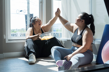 Two happy smiling Asian plus size woman eating snack during workout in fitness sport club. Young...