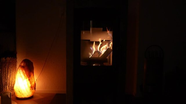 A warm and inviting scene with a cozy fireplace casting a warm glow on the room. The flickering flames dance within the hearth, illuminating a nearby salt lamp that emits a soft, rosy light.