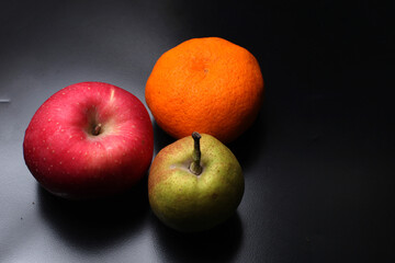An apple, pear, and orange isolated on black background, top view