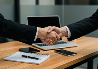 Business professionals shaking hands over a desk with financial contracts and documents in an office setting.