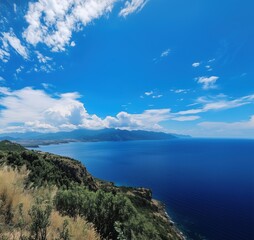 Fototapeta premium Breathtaking coastal view overlooking deep blue sea and distant mountains under a vibrant sky, copy space for text