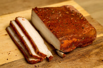 Ham with paprika and various spices on a wooden chopping board, with slices next to it.