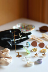 Hand figurine, sunglasses, gold jewelry, colorful bead jewelry, statement rings and various hair accessories on the white table. Selective focus.